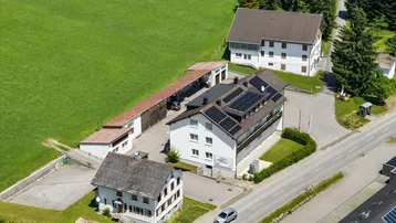 Luftaufnahme eines Anwesens mit mehreren Gebäuden, umgeben von grünen Feldern und einer Straße.