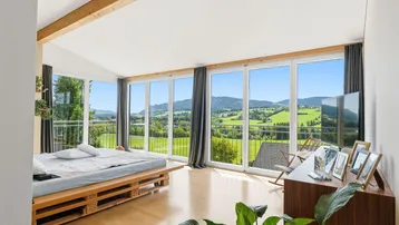 Helles Schlafzimmer mit Panoramafenstern, Holzbalken und weitem Blick auf die grüne Landschaft.