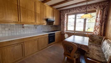 Traditionelle Wohnküche mit Holzschränken, Essbereich und Blick nach draußen durch das Fenster.