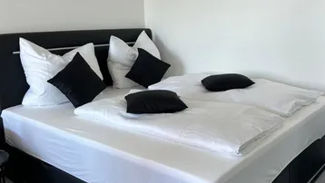Helles Schlafzimmer mit Doppelbett, weißer Bettwäsche und einem Teppich auf Fliesenboden.