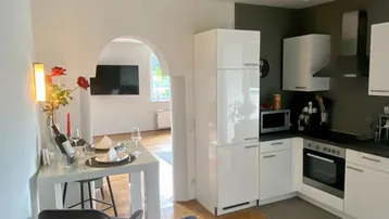 Moderne Küche mit weißen Hochglanzfronten, Holzboden und einem kleinen Essbereich mit Barhockern.