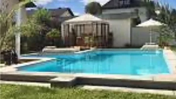 Großer Außenpool mit angrenzendem Gartenbereich und Pavillon unter blauem Himmel.