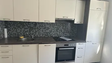 Funktionale Küche mit beigen Schränken, dunkler Arbeitsplatte und Mosaikfliesen als Spritzschutz.