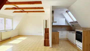 Heller offener Wohnbereich mit Parkettboden, sichtbaren Holzbalken und integrierter Küchenzeile unter Dachschrägen.