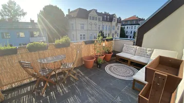 Sonnige Dachterrasse mit gemütlichen Sitzgelegenheiten und Blick auf die umliegenden Gebäude.