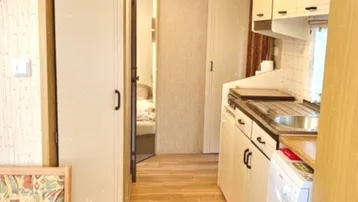 Schmale Küche mit Holzfußboden und Blick in angrenzende Räume, funktional eingerichtet.