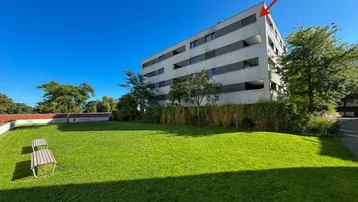Modernes Mehrfamilienhaus mit gepflegter Rasenfläche und Bäumen unter blauem Himmel.