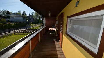 Überdachter Holzbalkon mit Blick auf die grüne Umgebung und die ruhige Wohnstraße.