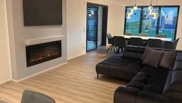 Offener Wohn- und Essbereich mit modernem Kamin, großem Sofa und Zugang zur Terrasse.