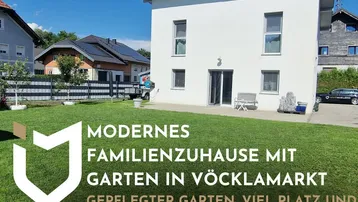 Modernes Einfamilienhaus mit weißer Fassade, gepflegtem Garten und kleiner Terrasse unter blauem Himmel.