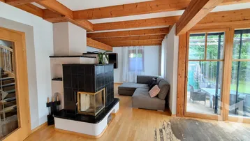 Gemütliches Wohnzimmer mit Kachelofen, Holzbalkendecke und Zugang zur Terrasse.