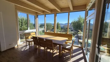 Heller Wintergarten mit Holzbalkendecke, großflächigen Fenstern und Esstisch mit Bergblick.