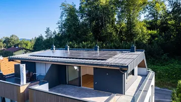 Dachterrasse mit Photovoltaikanlage und Blick auf die umliegende bewaldete Landschaft.