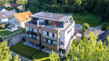 Moderne Wohnanlage mit Photovoltaikanlage auf dem Dach, umgeben von viel Grün und Bäumen.
