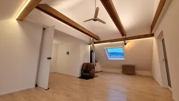 Geräumiger Dachgeschoss-Wohnbereich mit Holzbalken, Kaminofen und Dachfenster.
