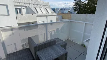 Geräumiger Balkon mit Rattanmöbeln und Blick auf die umliegenden Gebäude unter blauem Himmel.