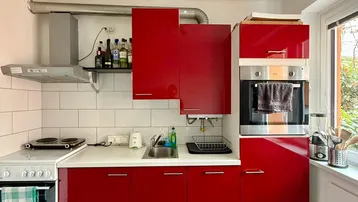 Helle Küche mit glänzenden roten Schränken, integriertem Backofen und Blick ins Grüne.