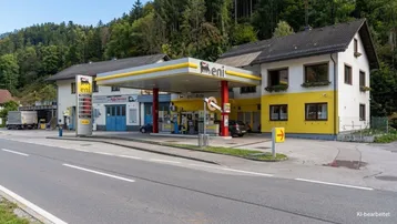 Außenansicht einer Tankstelle mit angrenzendem Gebäude und bewaldetem Hintergrund an einer Landstraße.
