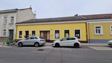 Gelbe Fassade eines Gebäudes an einer Straße mit parkenden Autos davor.