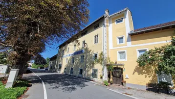 Gut erhaltenes, gelb gestrichenes Mehrfamilienhaus mit traditioneller Architektur und Satteldach, umgeben von Bäumen.