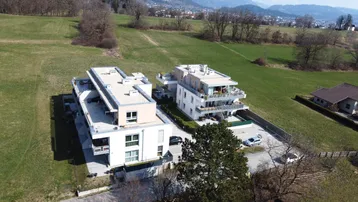 Luftaufnahme von modernen Wohngebäuden in einer grünen Landschaft mit Bergen im Hintergrund.