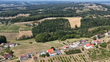 Luftaufnahme einer ländlichen Gegend mit Häusern, Feldern und Wäldern unter blauem Himmel.