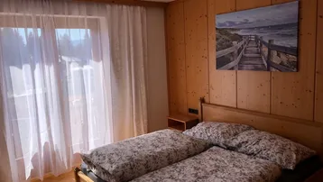 Helles Schlafzimmer mit zwei Einzelbetten, Holzwänden und Zugang zu einem Balkon.