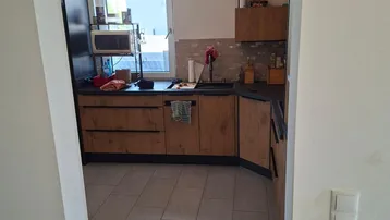 Moderne Küche mit Holzelementen, Einbaugeräten und Fenster mit Blick ins Grüne.