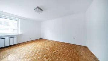 Helles Zimmer mit Fischgrätparkettboden, weißen Wänden und einem großen Fenster.