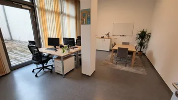 Modernes Büro mit zwei Arbeitsplätzen, einem Besprechungsbereich und Zugang zu einem Außenbereich.