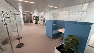 Moderner Bürogang mit blauen Sitznischen, Garderobe und Glaswänden, ideal für informelle Besprechungen.