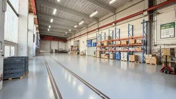 Geräumige Lagerhalle mit hohen Decken, Industrieboden und Regalsystemen für Lagerung von Waren.