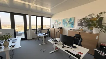 Helles und modernes Büro mit mehreren Arbeitsplätzen, großen Fenstern und weitem Ausblick auf die Landschaft.