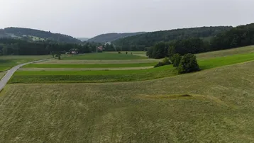 Luftaufnahme einer ländlichen Landschaft mit Feldern, Wäldern und einer Straße unter bewölktem Himmel.