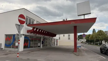 Außenansicht eines Geschäftsgebäudes mit großer Überdachung und Werbeschild unter bewölktem Himmel.