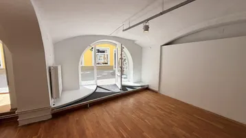 Heller Gewerberaum mit Holzboden und gewölbter Decke, direktem Zugang zur Straße und natürlichem Licht.