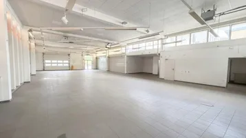 Geräumige, leere Gewerbefläche mit Fliesenboden, hohen Decken und viel Tageslicht durch große Fenster.