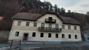 Altes Gebäude mit mehreren Balkonen und Ziegeldach, gelegen an einem bewaldeten Hang, renovierungsbedürftig.