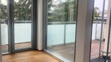 Heller Raum mit großen Fenstern, Holzboden und Zugang zu einer Holzterrasse.