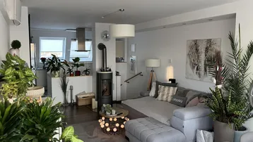 Helles, offenes Wohnzimmer mit gemütlichem Kaminofen, vielen Pflanzen und Zugang zur Küche.