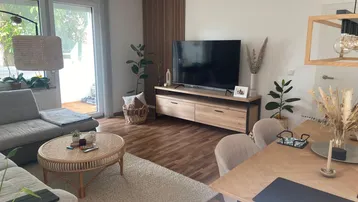 Helles Wohn- und Esszimmer mit Holzboden, modernem TV-Möbel und Zugang zum Balkon.