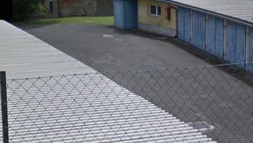 Außenbereich mit Garagenreihen, gepflastertem Hof und einem Zaun im Vordergrund.