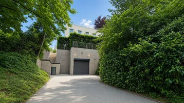Zufahrt zur Tiefgarage eines modernen Gebäudes, umgeben von üppigem Grün und Bäumen.
