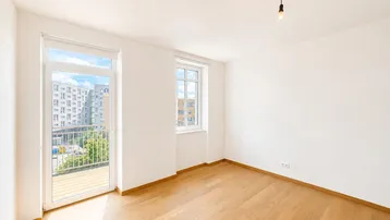 Helles Schlafzimmer mit Parkettboden und Zugang zu einem französischen Balkon.