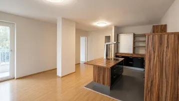 Heller offener Wohnbereich mit Holzboden und integrierter Küche, ideal für modernes Wohnen.