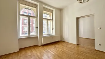 Geräumiges Zimmer mit Holzboden, großen Bogenfenstern und viel Tageslicht.