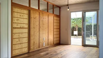 Heller Wohnraum mit Holzboden, Sichtbetondecke und großem Fenster zur Terrasse.