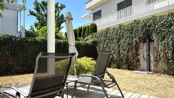Gartenbereich mit Rasenfläche, grünen Büschen und Blick auf die moderne Gebäudefassade.