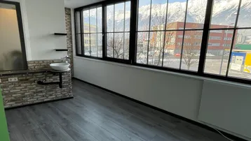Heller Innenraum mit großen Fenstern, die einen Blick auf schneebedeckte Berge bieten, und einem Waschbecken an der Wand.