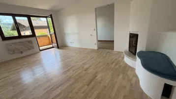 Helles Wohnzimmer mit Holzboden, Kamin und Zugang zu einem Balkon mit Blick ins Grüne.